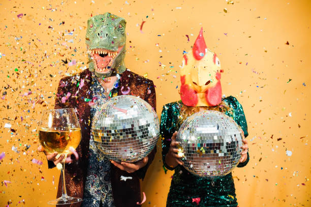 crazy couple having fun holding disco balls and champagne glass at party - focus on chicken mask - bizar stockfoto's en -beelden