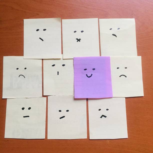 istock Concept for a positive attitude with a small office note with many faces and one that stands out with a smile. Smile when the situation is bad. 1359671555