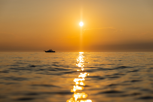 Beautiful sunset over the sea casting light beam reflection on the water,visible waves,single small ship on the horizon next to the sun,horizontal