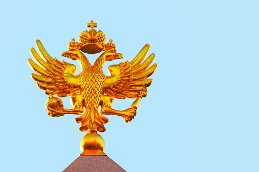 Golden russian double-headed eagle on a blue sky background at sunny day, front view