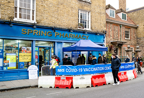 London, UK - 17 December, 2021: people waiting in line to receive their Covid-19 vaccinations and booster jabs outside a pharmacy in London, UK.