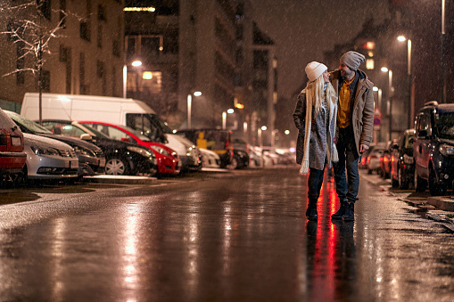 Happy young man and woman walking in a beautiful city in the snowy night