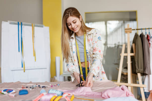 istock Young smiling girl dreamily using scissors for work with fabric in sewing workshop 1359677639