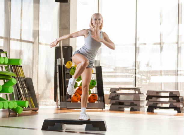 jeune belle femme avec un corps parfait faisant des exercices sur le stepper d’escalier dans la salle de gym. aérobic intense. concept de mode de vie sain. - in step photos et images de collection