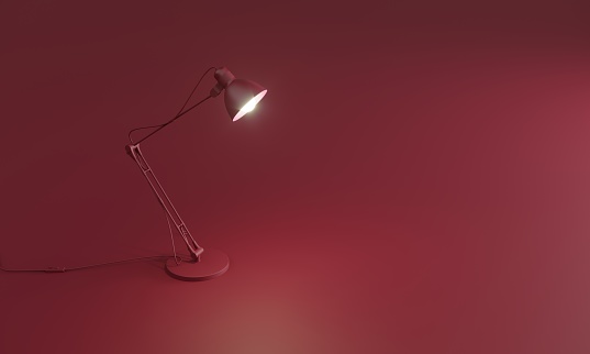 Modern glowing desk lamp is standing on red background.