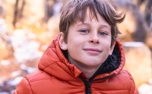 A boy with a slight smile looks confidently at the photographer in the winter forest in the mountains during a hike. Portrait of a white Caucasian boy 8 years old