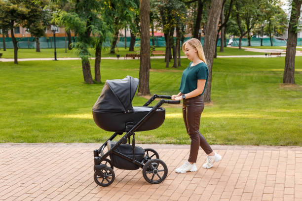 istock Young blonde woman walking with black stroller in summer park 1359683465