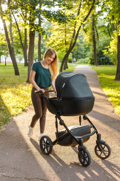 istock Young blonde woman walking with black stroller in summer park 1359683476