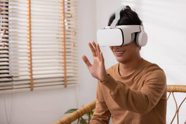 istock Asian man wearing virtual reality goggles in modern coworking studio. Smartphone using with VR headset. 1359684221