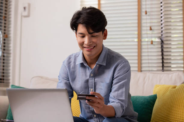 istock Asian man makes a payment via the internet. On the sofa at home, a shopper shops online using a credit card and a smartphone. The concept of internet shopping. 1359684230