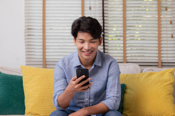 istock Sitting on the sofa in the house, an Asian man works on his smartphone.Man works while using social media applications. The concept of working from home. 1359684246