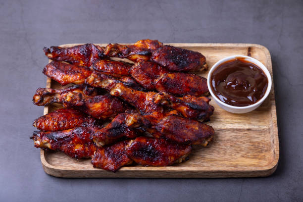 ailes de poulet frites sur une planche en bois avec sauce barbecue. fond noir, gros plan - rotisserie chicken barbecue grill food photos et images de collection