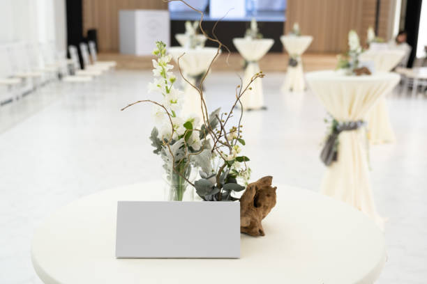 istock Tent cards placed on a tall table covered with white cloth decorated with twigs and white flowers at a wedding banquet in a hotel. 1359688350