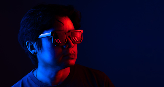 Asian man wearing fashion sunglasses in dark blue and red light with copy space