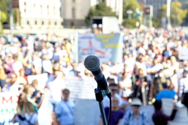 istock Protest or public demonstration, focus on microphone, blurred crowd of people in the background 1359691415