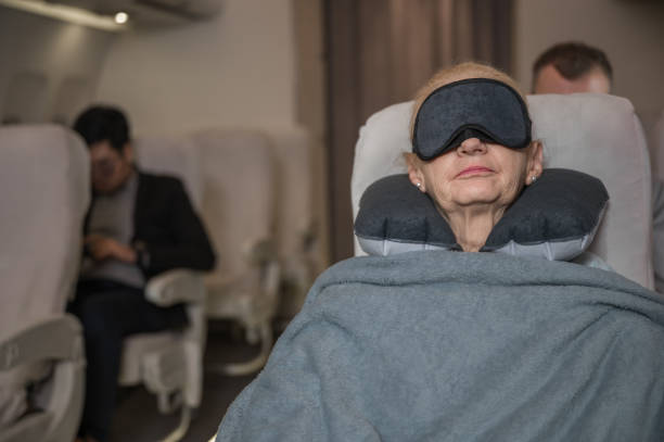 счастливая пожилая женщина-пассажир использует маску с завязанными глазами и подушку на шее с удобным одеялом, пока спит на сиденье самоле� - personal flotation device стоковые фото и изображения
