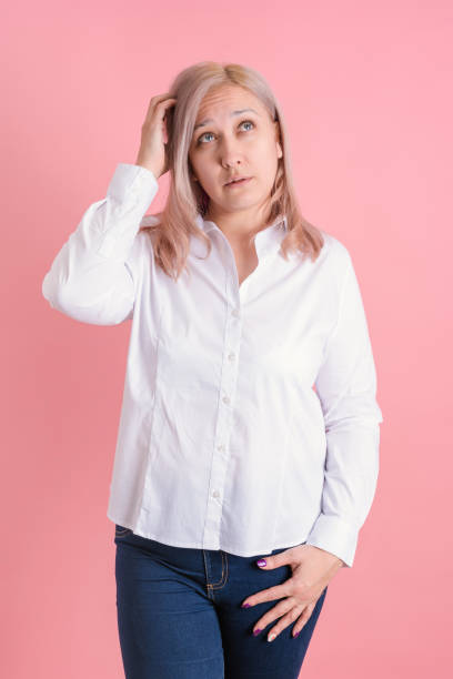 istock A 40s woman thoughtfully scratches her head while standing on a pink background 1359703661