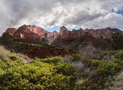 An outdoor landscape of a red mountain surrounded by lush trees and billowy clouds.