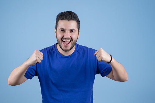 Young excited man waving his hands into fists against a blue background. ambitious and successful man