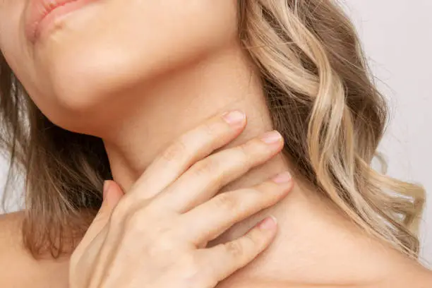 A cropped shot of a young blonde woman touching the neck with her hand hiding wrinkles, age-related changes, lines isolated on a white background. Sore throat