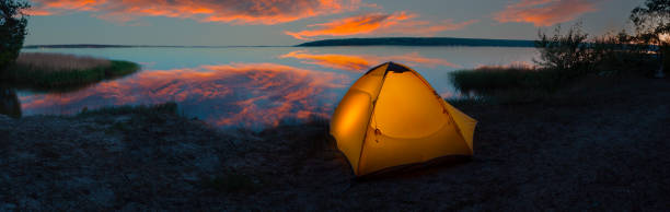 istock Orange tourist tent illuminated from inside on the lakeside under dramatic sky 1359711094