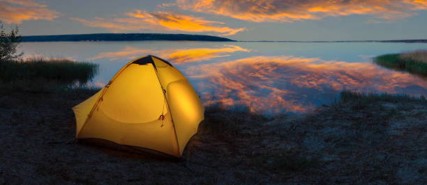 istock Orange tourist tent illuminated from the inside on the lakeside under dramatic sky 1359711228
