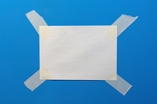 A blank white sheet of paper is attached with paper duct tape to a blue mill. Form for the announcement. Background. Texture.