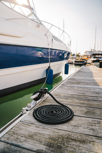 A large blue and white striped boat is tied with a lack dock line to the deck at the marina