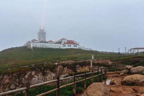 Photo of Wooden fence puddle and luminous lighthouse at Cape Roca