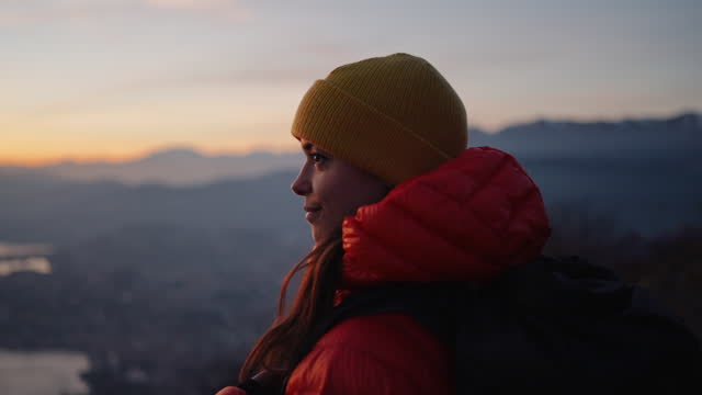 Female hiking standing on mountain top enjoying fresh air and view of lake, sunset and city below