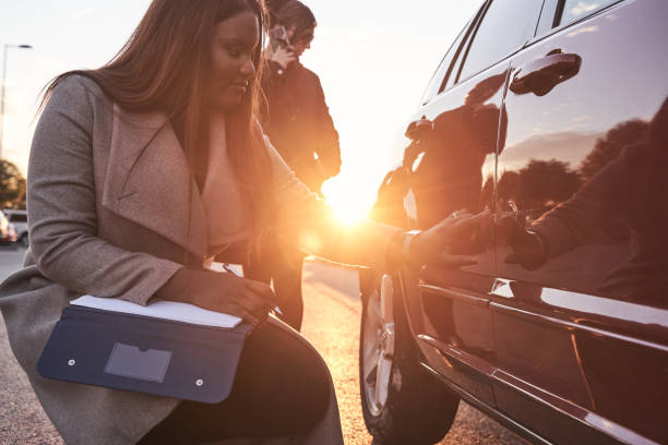 insurance agent examines the car while the driver talks on the mobile phone. accident claim process. african-american woman checking the damage to the car after an accident. concept of transportation. - car insurance insurance agent damaged imagens e fotografias de stock