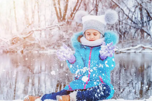 Child at winter. Happy girl outdoors.Funny little girl having fun in beautiful winter park.Child playing with snow in winter. Little girl in catching snowflakes in winter park on Christmas.