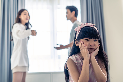 Asian little girl crying while parents fighting or quarrel conflict. Young kid daughter sit on bed feel heart broken with tears and dont want to see violence at home. Family problem-separation concept