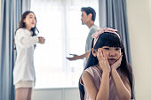 Asian little girl crying while parents fighting or quarrel conflict. Young kid daughter sit on bed feel heart broken with tears and dont want to see violence at home. Family problem-separation concept