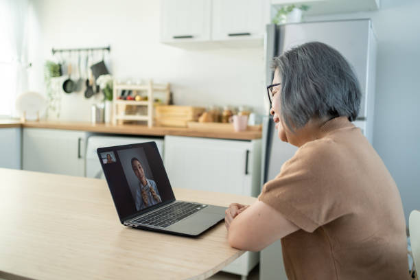 Asian senior older woman video call with doctor in living room at home. Elder patient consulting with general practitioner application computer laptop. Doctor and Consultant online and telemedicine. stock photo