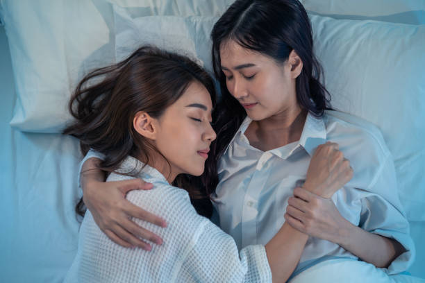 istock Asian beautiful lesbian couple lying down on bed and hugging each other. Attractive romantic girl friend in pajamas spending night leisure time together in bedroom in house 1359757928