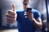 Shot of an unrecognisable man showing using a smartphone and showing thumbs up in a gym