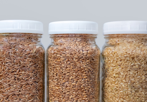 Food storage glass containers are filled with: whole grain farro, whole grain wheat and brown short  grain rice. Hard grains for emergency food supply.