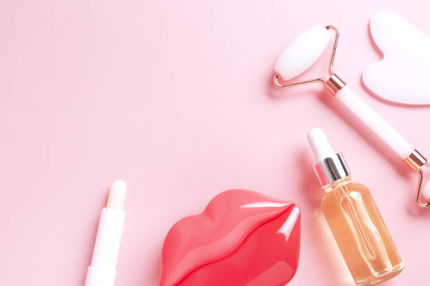 istock Beautiful composition of unbranded serum bottle, face roller, guasha on pink background. Lips skin care. Creative trendy cosmetics flat lay with copy space 1359784942