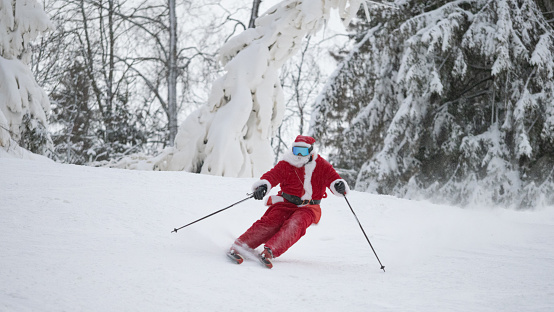 Santa Claus alpine skier skiing downhill in snowy forest ski resort slope Christmas sport lifestyle celebration