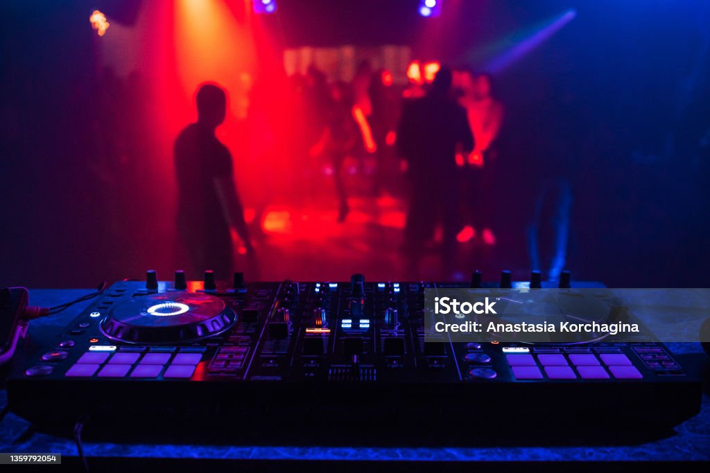 DJ console for mixing music with blurry people dancing at a nightclub party DJ console mixing music blurry people dancing nightclub party DJ Stock Photo