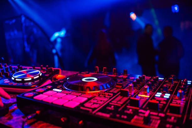 DJ console for mixing music with blurry people dancing at a nightclub party DJ console mixing music blurry people dancing nightclub party dj photos stock pictures, royalty-free photos & images