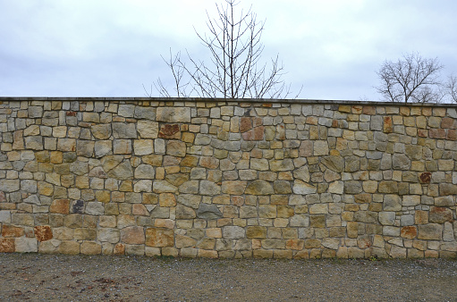 The plank fence follows the sandstone-lined wall that is cracking in several places, the movements of the terrain and the vibrations of the highway car traffic. grassy slope and high wall sloping down