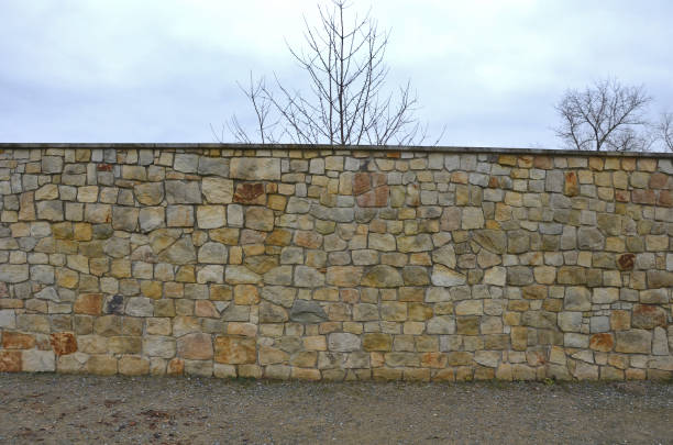 The plank fence follows the sandstone-lined wall that is cracking in several places, the movements of the terrain and the vibrations of the highway car traffic. grassy slope and high wall sloping down The plank fence follows the sandstone-lined wall that is cracking in several places, the movements of the terrain and the vibrations of the highway car traffic. grassy slope and high wall sloping down walled garden stock pictures, royalty-free photos & images