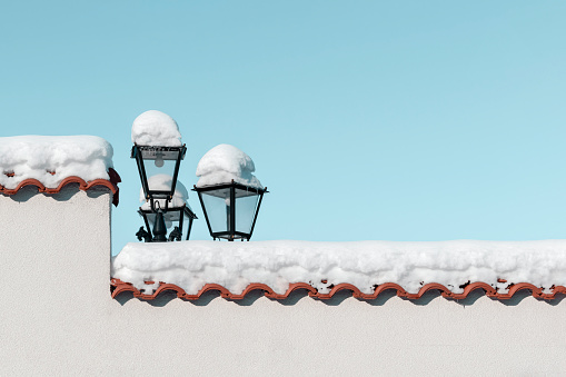 Winter scene. Snow on stone fence of house and lantern, clear blue sky on frosty sunny day on street of town. Snowing on terracotta roof tiles. Minimalistic winter concept, background, copy space