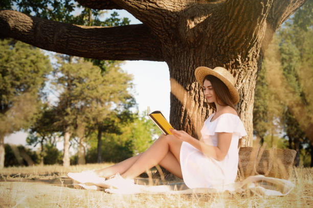 istock Young woman reading book near tree in park 1359799598