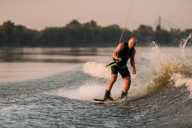 istock active man holds cable and energetically rides down on splashing wave on wakeboard. 1359805433