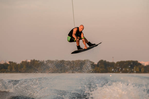 istock muscular man holds cable and masterfully jumping above splashing wave on wakeboard. 1359806141