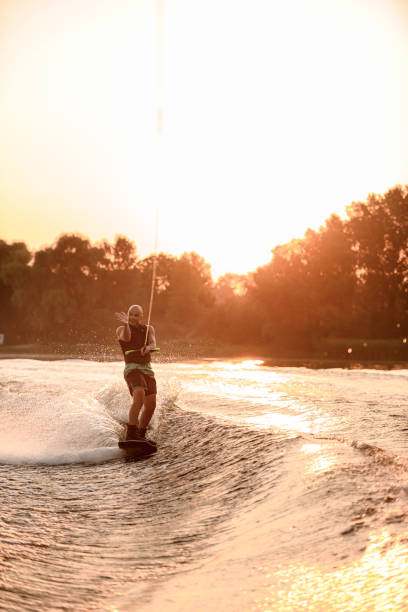 istock Cheerful man holds cable and rolls on water on wakeboard on a sunset background 1359806361