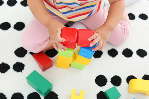 Cute little girl playing with colorful cubes on floor indoors, above view. Educational toy